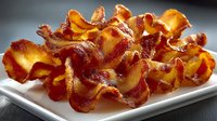 Crispy golden bacon strips perfectly cooked and arranged on white plate. High-protein breakfast meat ready for morning meals and culinary projects.