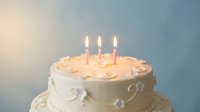 Birthday cake with three lit candles and white frosting decorative swirls on gradient background for celebration party dessert baking concepts.