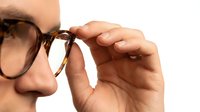 Man adjusting tortoiseshell eyeglasses on white background, isolated for design use on apparel, marketing materials, and optical retail applications.