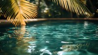 Tranquil swimming pool with turquoise water reflecting golden palm fronds, creating a tropical resort atmosphere for luxury vacation advertising.