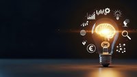 Glowing light bulb with business icons and charts floating around, representing innovation, creativity and entrepreneurial ideas on dark background.
