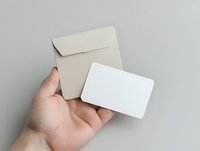 Caucasian male hand holding blank cream envelope and white business card on neutral background for branding and corporate identity mockup design.