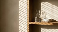 Wooden shelf with glass bottles and containers against beige wall with natural sunlight casting striped shadows, suitable for minimalist home decor and interior design projects.