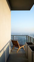 Modern high-rise balcony with wooden lounge chair overlooking urban cityscape, ideal for real estate, hospitality, and lifestyle design projects.