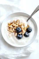Fresh blueberries and pine nuts on creamy yogurt with cinnamon sprinkle in white ceramic bowl, healthy breakfast or snack on light background.