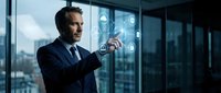 Professional businessman in dark suit interacting with futuristic holographic interface in modern office with city skyline view through windows.