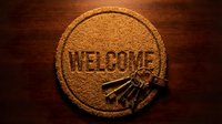 Round welcome doormat with vintage keys on wooden floor, symbolizing new home ownership, real estate, and hospitality concepts.