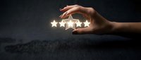 Hand holding five glowing stars against dark background, representing customer satisfaction, quality rating, and positive feedback for business and service excellence.