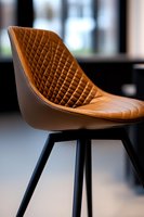 Modern brown leather bar stool with quilted diamond pattern upholstery and black metal legs against blurred background, showcasing contemporary furniture design.