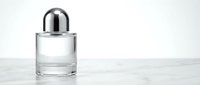 Elegant clear glass perfume bottle with silver cap on white marble surface, minimalist luxury fragrance container for cosmetic and beauty product design.