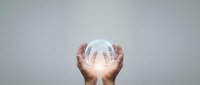 Hands cupping glowing transparent sphere with bright light emanating from center against neutral gray background for business and technology concepts.