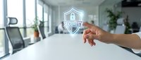 Hand pointing at glowing security shield icon in modern office environment representing cybersecurity protection and data safety solutions for business.