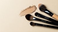 Professional makeup brushes with loose beige powder foundation smear on neutral background, essential cosmetic tools for beauty artists and makeup application.