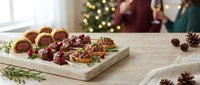 Festive holiday appetizer platter with gourmet canapes and meat rolls on wooden board. Christmas party food spread with pine cones and decorations.