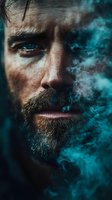 Close-up portrait of bearded man with intense blue eyes partially obscured by turquoise smoke, creating mysterious atmospheric effect.