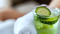 Fresh cucumber cocktail with sparkling water and ice cubes in glass, garnished with sliced cucumber. Refreshing summer drink against blurred background.