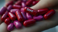 Red and pink capsule pills with love text scattered on surface, romantic medical concept for relationship therapy and emotional healing. Selective focus on foreground.