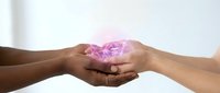 Two diverse hands gently cupping glowing pink heart with sparkles, symbolizing love, care, unity and compassion in healing relationship concept.