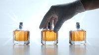 Gloved hand arranging luxury perfume bottles with golden fragrance on white background, showcasing elegance for beauty and cosmetic advertising.
