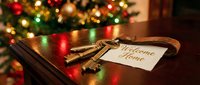 Vintage keys with a welcome home tag on a wooden table near a decorated Christmas tree, symbolizing new home ownership during the holiday season.