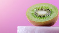 Fresh juicy kiwi fruit half showing detailed seed pattern and vibrant green flesh on white surface against pink background, macro food photography.