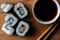 Fresh sushi rolls with cucumber and cream cheese served on wooden surface with soy sauce and chopsticks, top view composition for food photography.