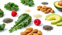 Healthy superfood ingredients including kale, avocado, almonds, chia seeds, quinoa and strawberries arranged on white background for clean eating concept.