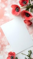 Coral pink anemone flowers frame blank white paper on marble background with soft pink watercolor texture, creating elegant flat lay composition for stationery design.