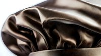 Luxurious brown silk fabric with soft folds and waves creating elegant drapery texture, smooth satin material with glossy sheen and gentle shadows.