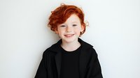 Cheerful redhead Caucasian boy with curly hair smiling confidently in black outfit against white background, studio portrait.