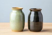 Handcrafted ceramic vases with glazed finish in green and dark brown colors on wooden surface against neutral background.