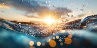 Dramatic ocean wave splash with water drops against golden sunset sky, creating dynamic motion and bokeh effect. Underwater perspective captures light rays.