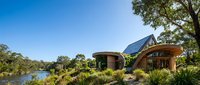 Modern eco-friendly house with solar panels overlooking serene lake surrounded by native vegetation under clear blue sky for sustainable living concepts.