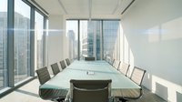 Modern conference room with long white table, black leather chairs, and floor-to-ceiling windows overlooking city skyline. Corporate meeting space for business presentations and team gatherings.