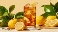 Refreshing iced tea with lemon slices in glass surrounded by fresh citrus fruits and green leaves on warm yellow background.