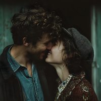 Young couple sharing intimate moment with foreheads touching in moody lighting. Romantic connection between curly-haired man and woman expressing love and tenderness.