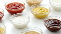 Assorted condiment sauces in glass bowls including mayonnaise, mustard, ketchup and barbecue sauce on white background, ready for food styling and culinary design projects.
