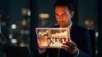 Professional businessman analyzing financial data on transparent tablet screen with glowing charts and graphs in modern office at night.