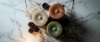 Scented candles in copper, cream, and sage green arranged with dried botanicals on marble surface for home decor and wellness styling.