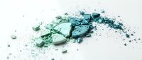 Crushed eyeshadow powder in shades of teal and green scattered on white surface, suitable for cosmetics, beauty product photography, and makeup tutorials.