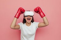 Excited young woman wearing VR headset and red boxing gloves celebrating victory on pink background. Virtual reality gaming and sports training concept.