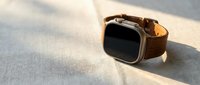 Modern smartwatch with brown leather strap on textured surface with dramatic shadow lighting for technology and lifestyle concepts.