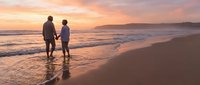 Romantic couple holding hands walking on beach at sunset with golden sky and ocean waves creating peaceful moment for love and togetherness.