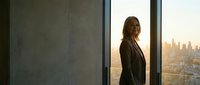 Professional businesswoman in suit standing by office window overlooking city skyline at sunset, corporate success and leadership concept.