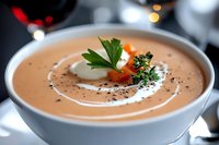 Creamy bisque soup garnished with fresh herbs, cream swirl, and diced vegetables in white bowl, elegant restaurant presentation against dark background.