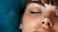Close up macro shot of young Asian woman with closed eyes, natural makeup, long eyelashes and smooth skin against blue background, expressing serenity and relaxation.