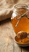 Golden honey jar with wooden dipper on rustic table for natural sweetener cooking baking organic food preparation kitchen ingredients healthy lifestyle.