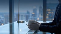 Business professional holding coffee cup by office window overlooking city skyline at dusk for corporate lifestyle and workplace concepts.