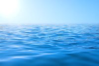 Calm blue ocean surface with gentle ripples stretching to horizon under clear sky and bright sun, creating serene seascape view for nature backgrounds.