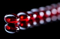 Red transparent gel capsules or pills arranged in line with reflection on black glossy surface, dramatic lighting creates medical or pharmaceutical mood.